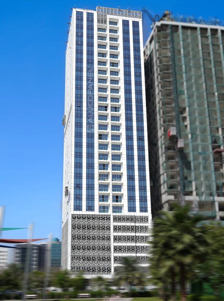 Construction workers on a suspended cradle platform finishing Alucopanel ACM cladding and curtain wall glazing at the corner of a high-rise building with a geometric podium screen below